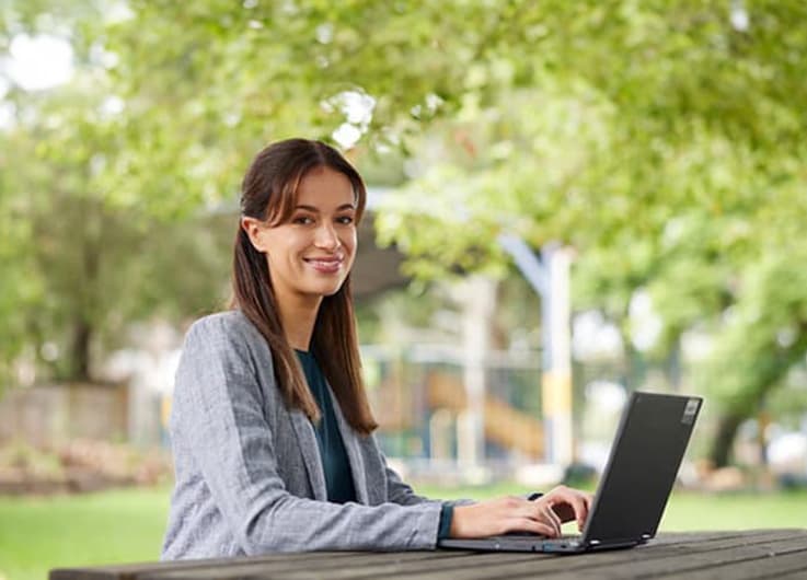 young woman sitting at a table with a laptop looking at the camera and smiling